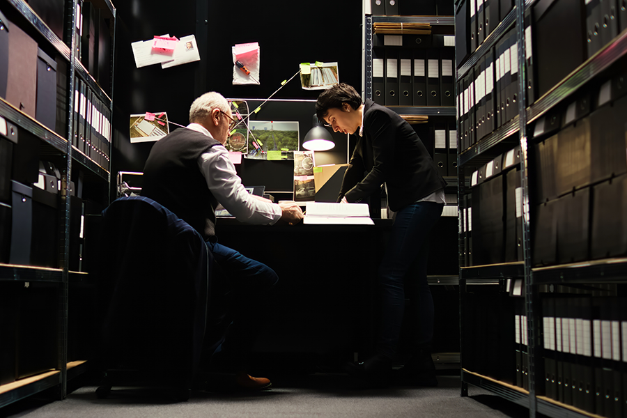 Two people in a room full of file boxes examining pages.