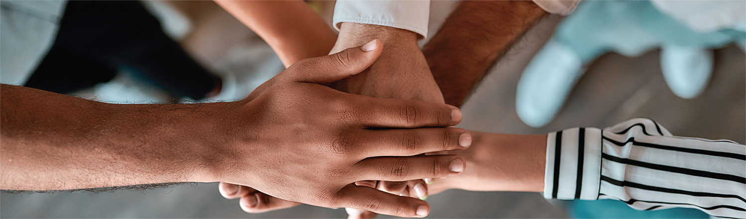 Several people putting their hands on top of one another in the middle of their circle.